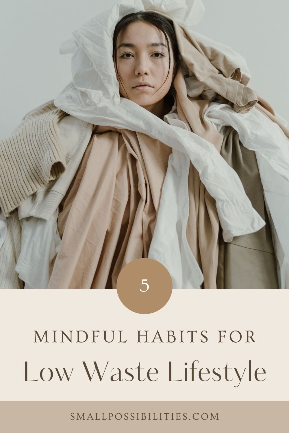 Young woman wrapped in neutral-toned clothing, visually overwhelmed by fabric, representing emotional weight of excess consumption and the call for low waste lifestyle changes.